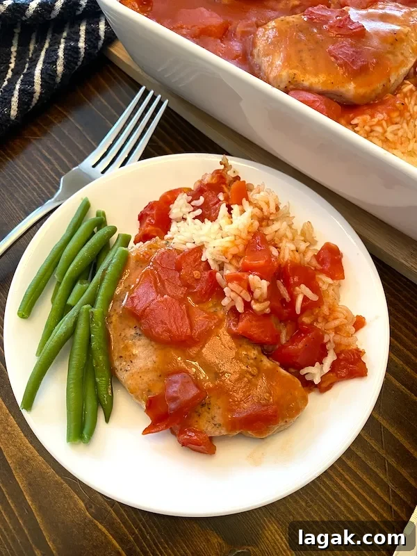 a serving of pork chop casserole with tomato gravy on a white plate next to green beans.