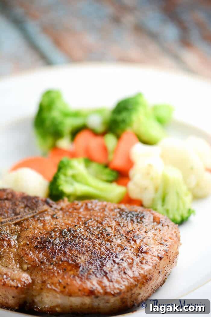 a seasoned pork chops on a plate with steamed veggies.