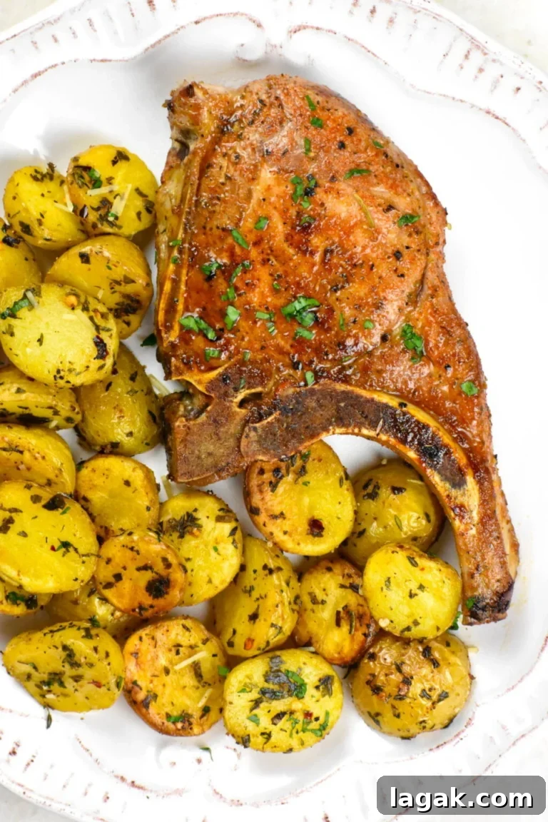 a baked bon-in pork chop on a plate next to roasted potatoes.