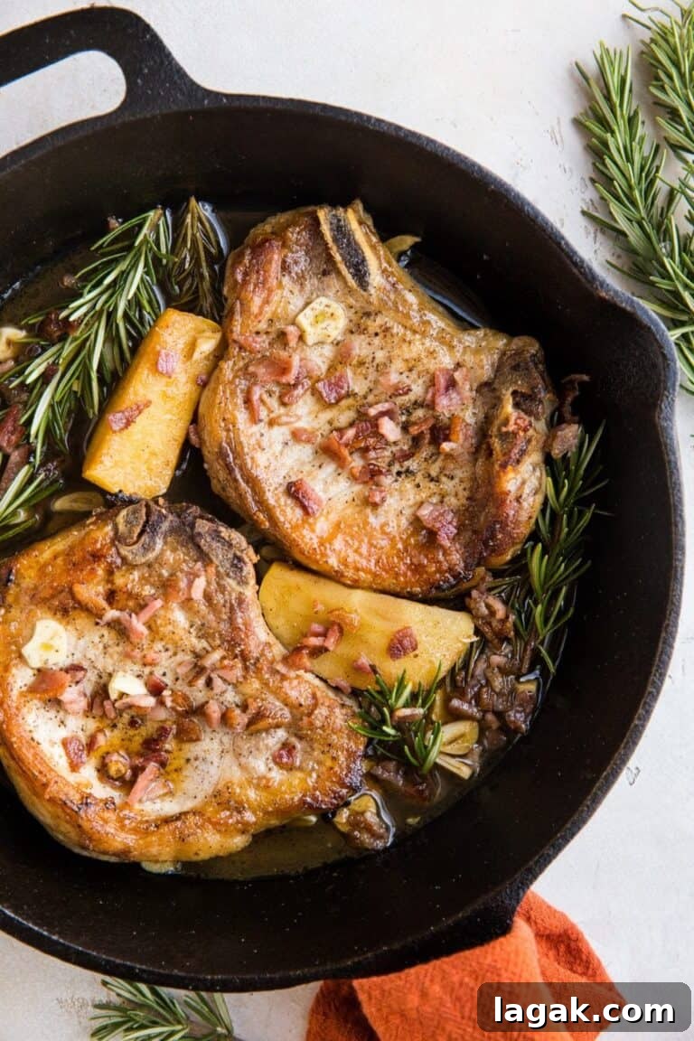 two pork chops in a skillet with rosemary, apples and bacon.