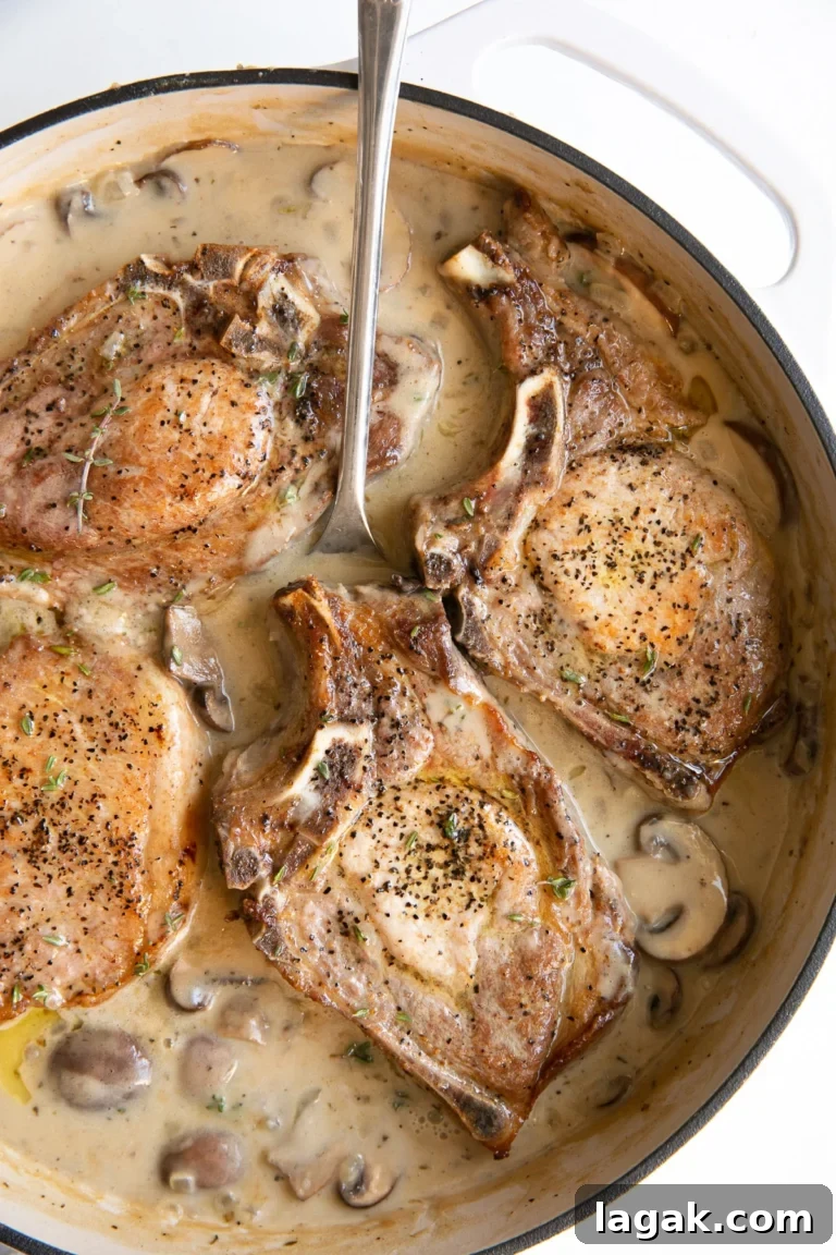 four smothered pork chops in a baking dish with a spoon inserted into the sauce.