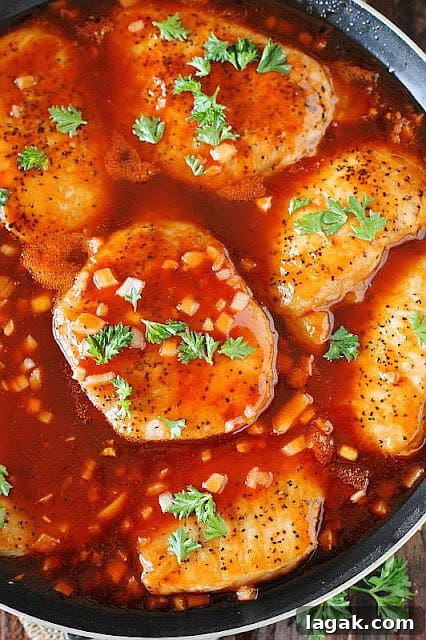 several pork chops in a pan simmering in sweet BBQ sauce.