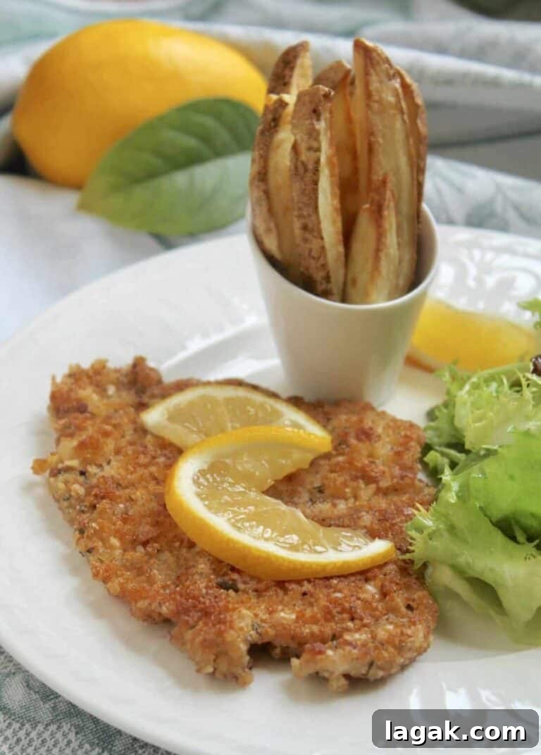 a pork schniztel cutlet on a plate with lemon, salad, and fries.