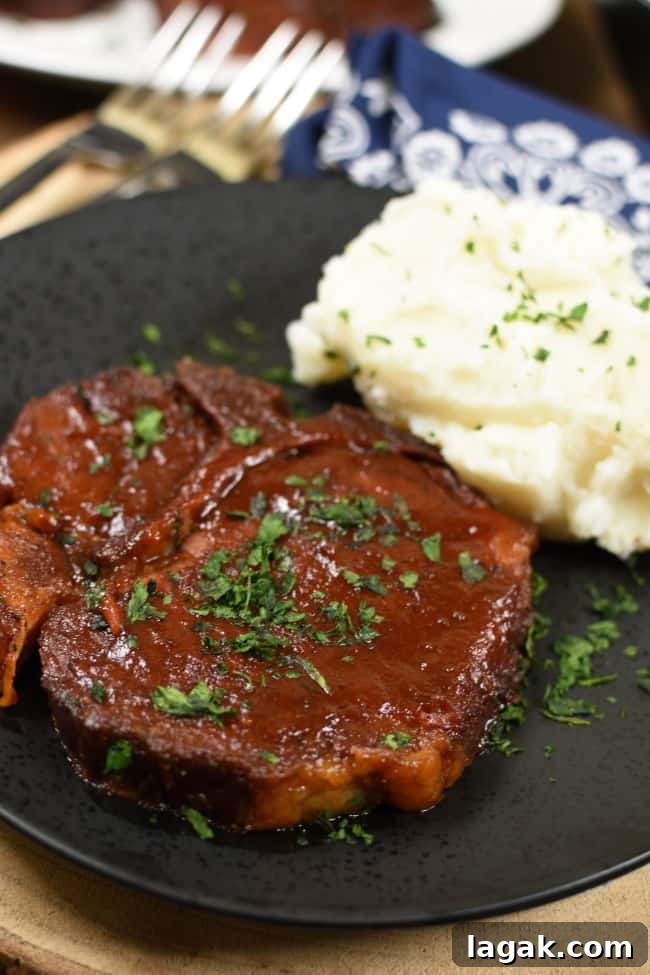 2 BBQ pork chops on a black plate next to a pile of mashed potatoes.