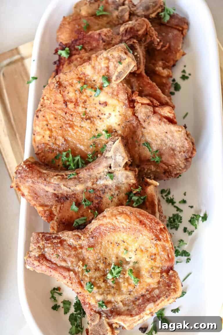 several fried pork chops sprinkled with parsley on white serving platter.