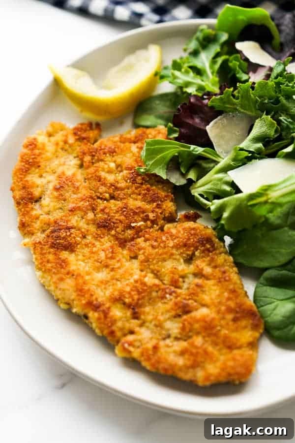 a piece of pork milanese on a white plate next to a green salad.