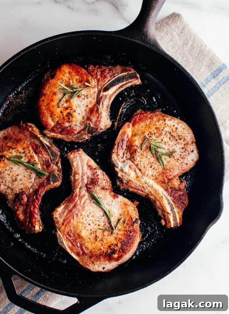 four bone-in pork chops in a skillet with rosemary sprigs.
