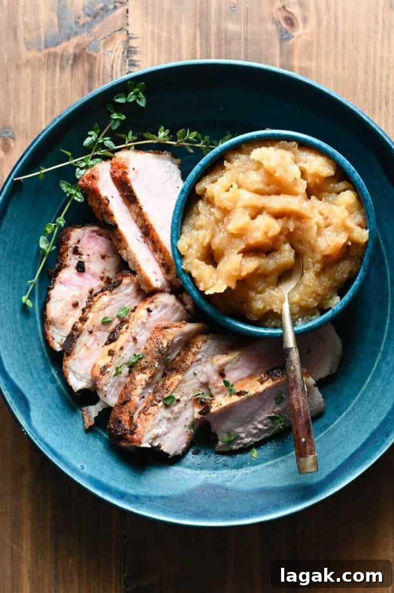 sliced pork chops on a blue plate next to a bowl of applesauce.