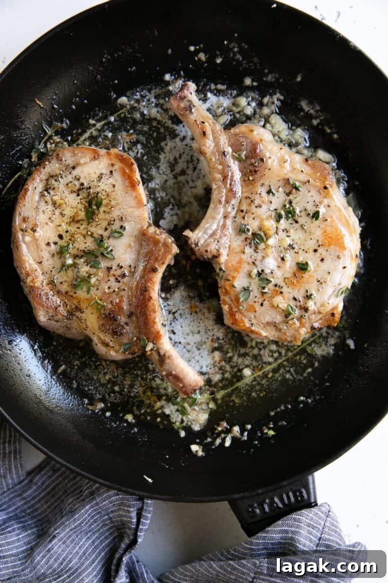 two bone-in pork chops in a frying pan with garlic butter.