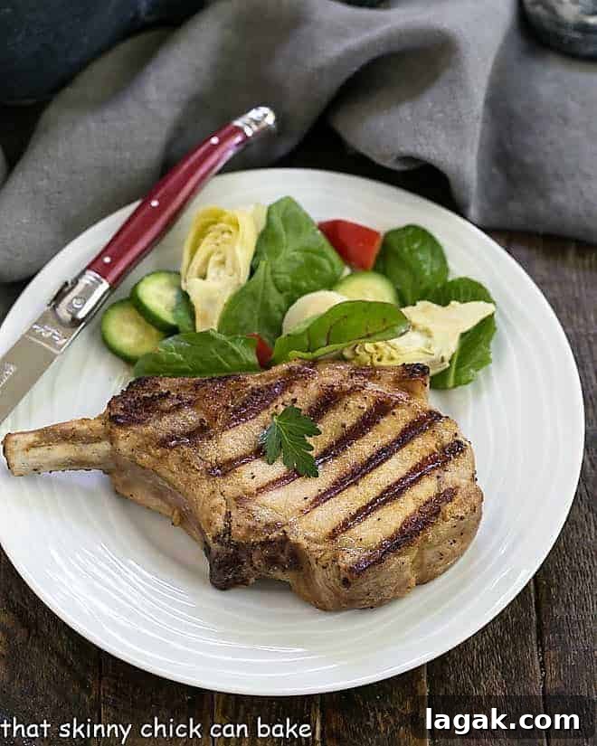 a pork chop on a white plate next to a knife and salad.