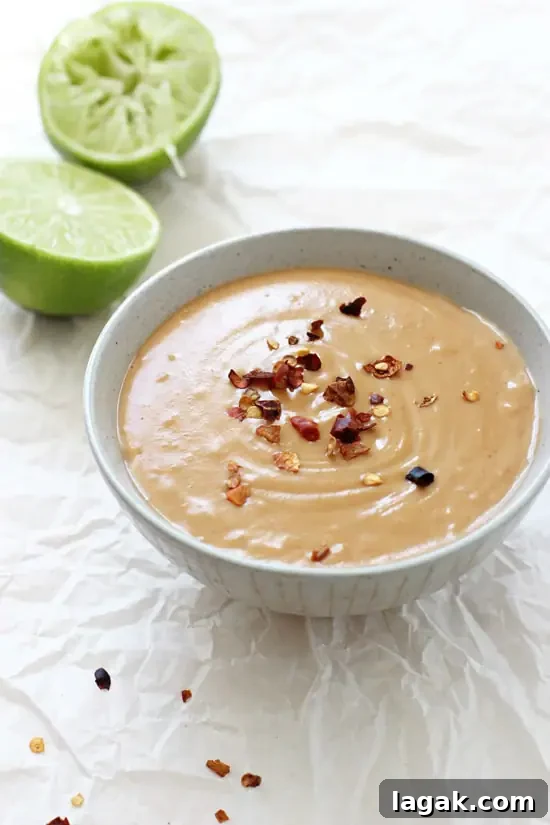 This 15 minute homemade peanut sauce is packed with flavor and healthier than the stuff from the store! Use as a dipping sauce, in stir-fries or however you like! A grey bowl filled with Homemade Thai Peanut Sauce with lime halves in the background.