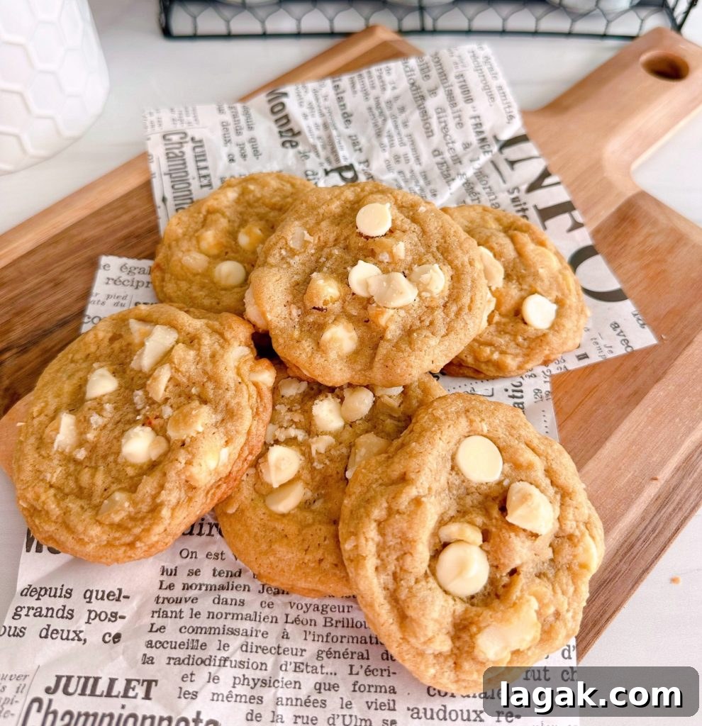 White Chocolate Macadamia Pudding Cookies Recipe 9 White Chocolate Chip Macadamia Nut cookies in a pile on a cutting board with news paper print.