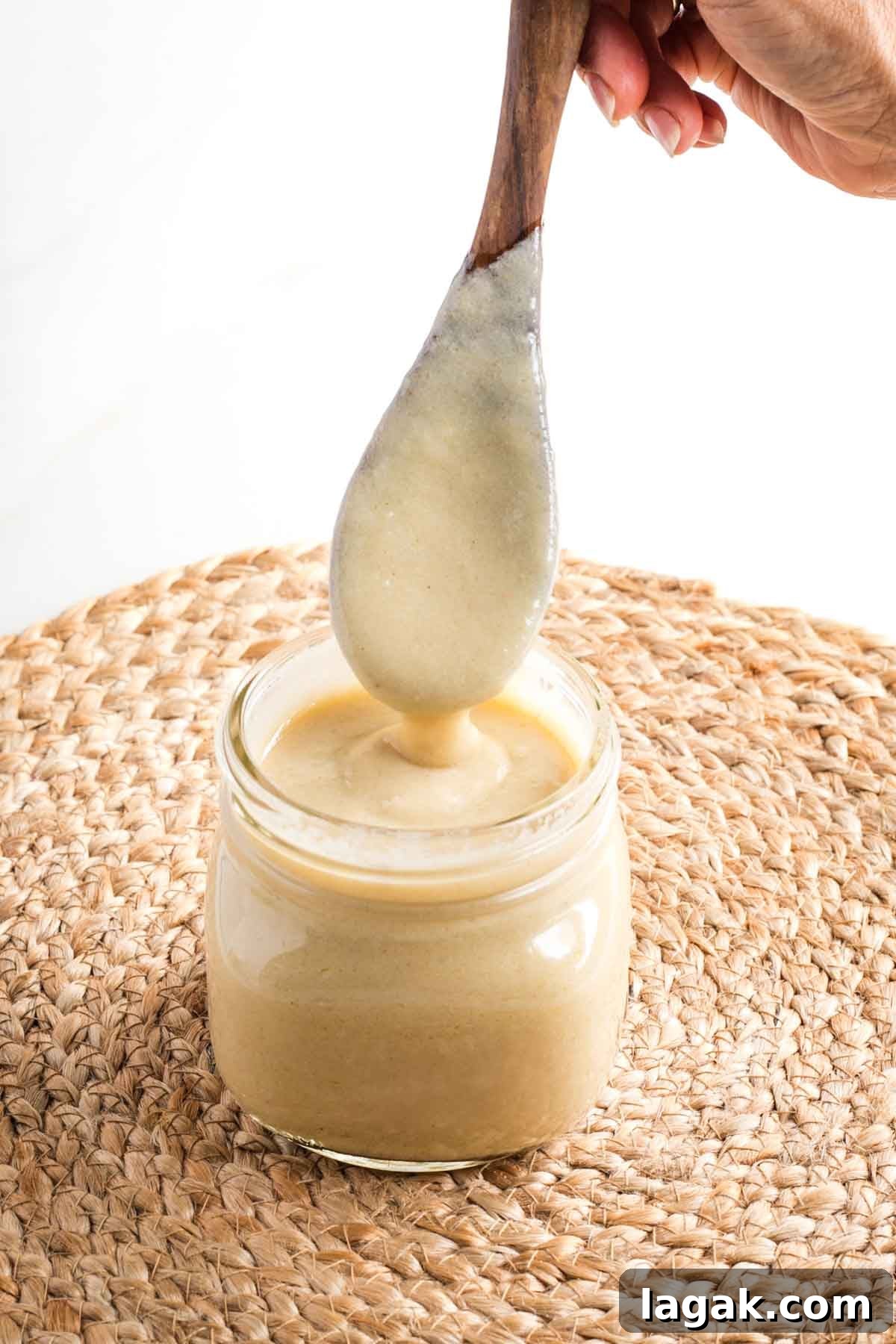 Wooden spoon, coated with bechamel sauce, coming out of a jar, showing how thick sauce is. 