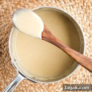 Bechamel sauce clinging to a wooden spoon resting atop a saucepan filled with the white sauce.