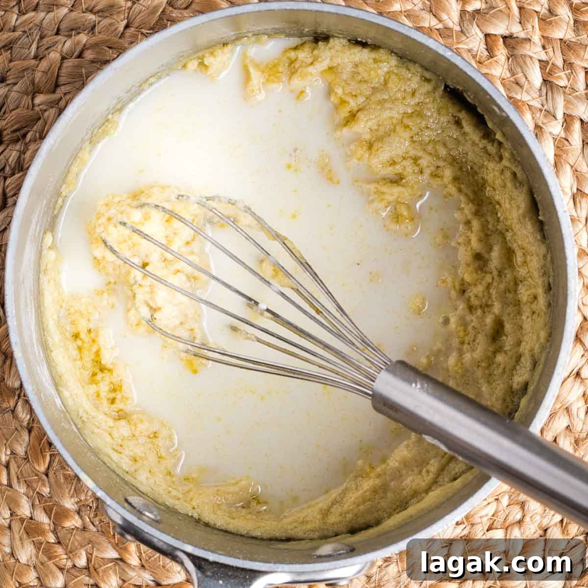 Whisking milk into a thick and pasty light yellow mixture in a saucepan.