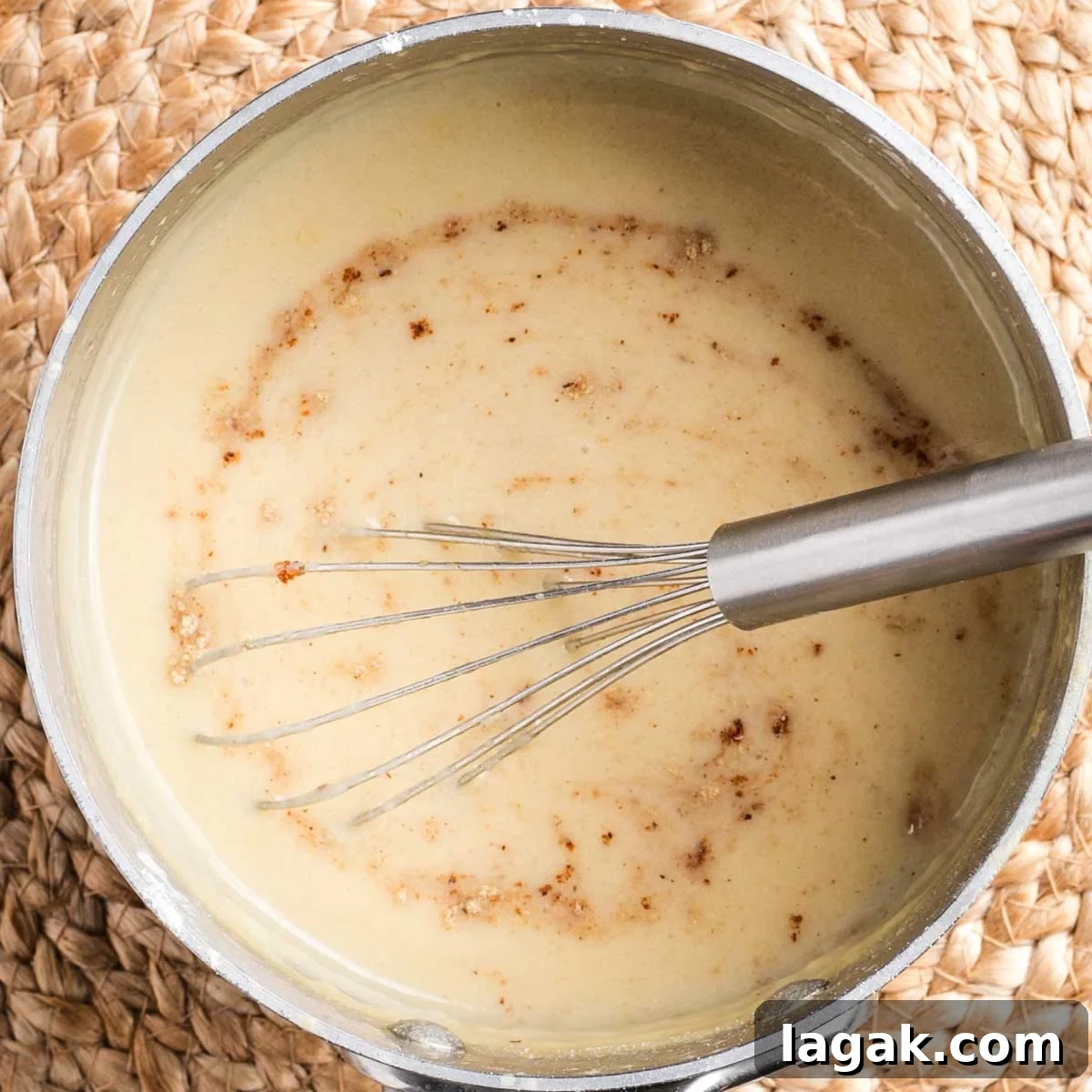 Whisking nutmeg into a light yellow thick sauce in a small saucepan.