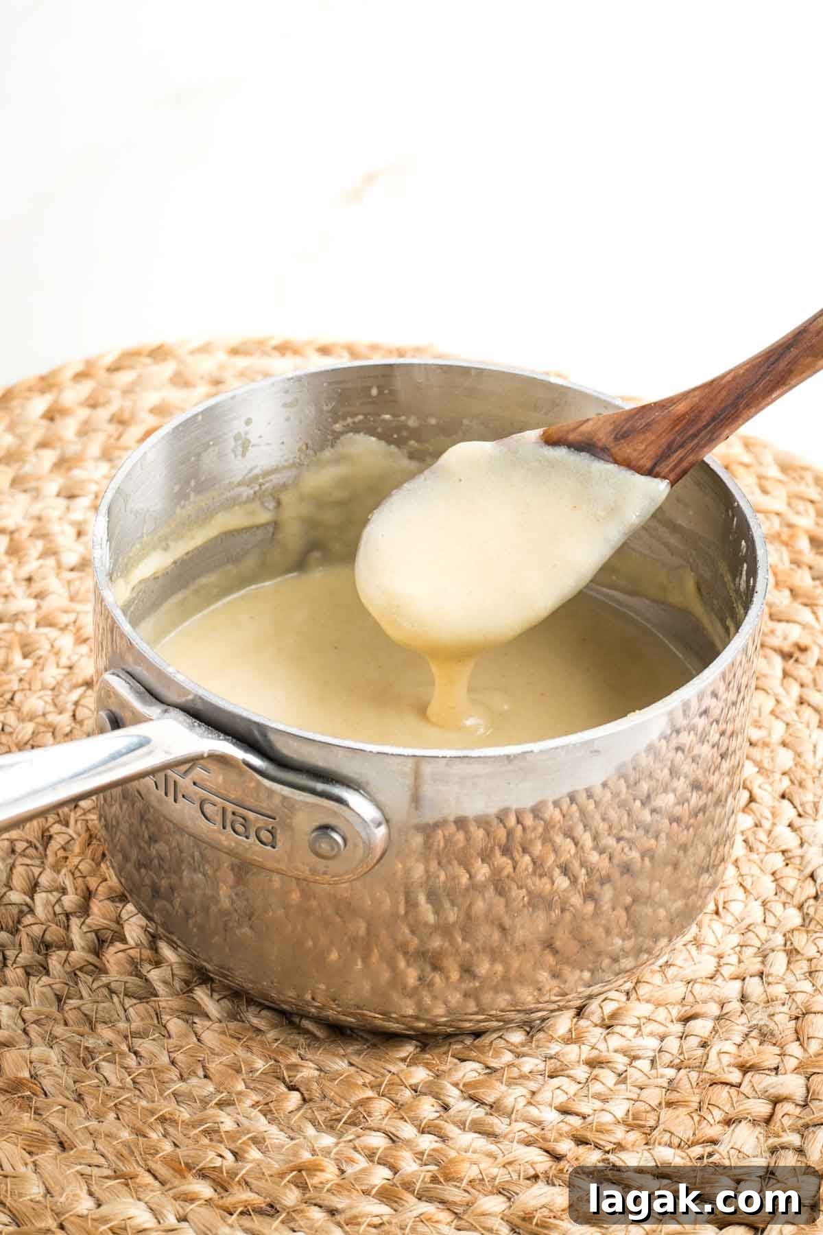 Wooden spoon peeking out of a saucepan full of white sauce to show how thick it is. 