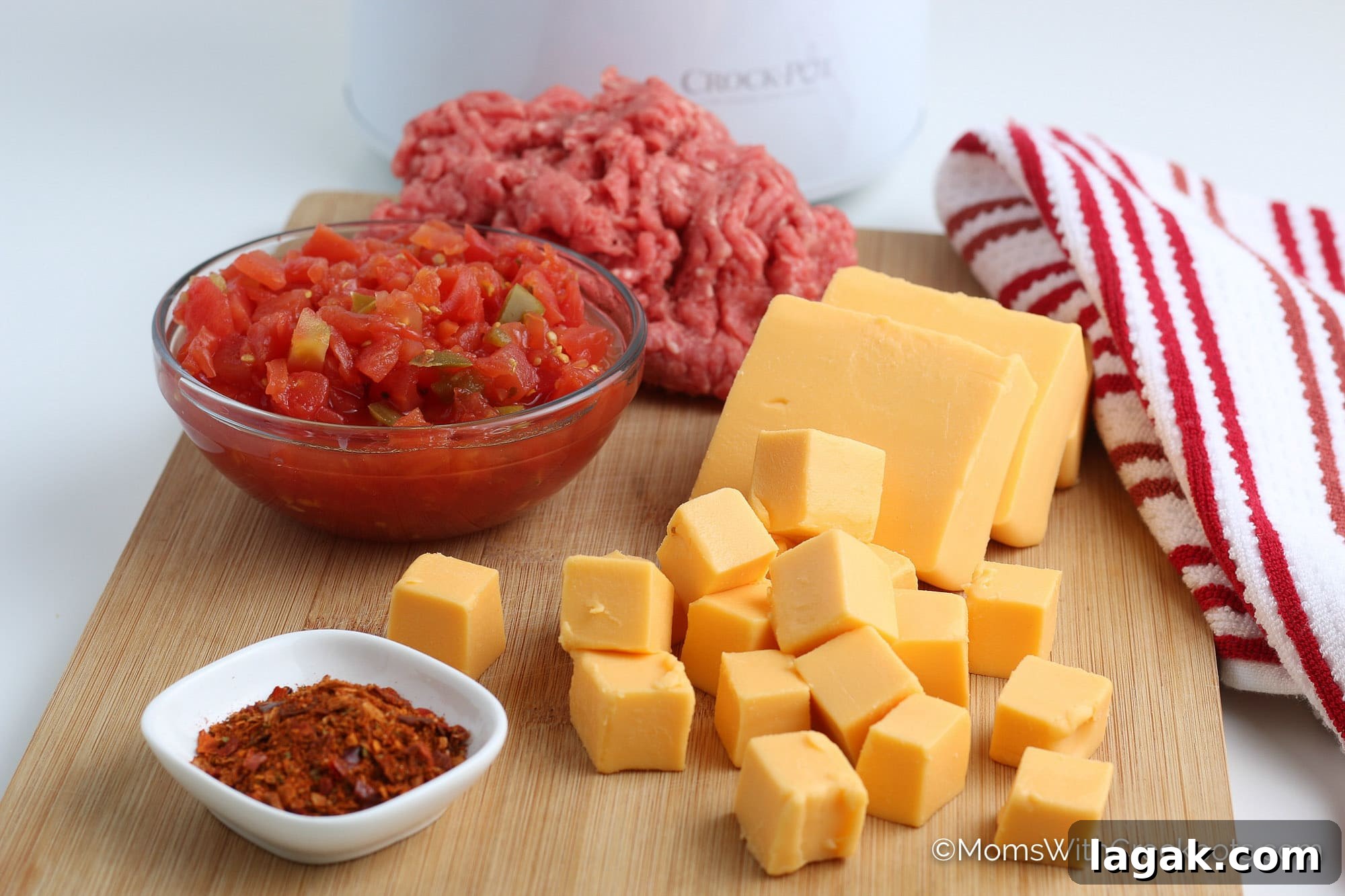4-Ingredient Crockpot Rotel Dip Recipe for Game Day 3 Velveeta, Taco Seasoning , Rotel Tomatoes, and ground beef on cutting board.