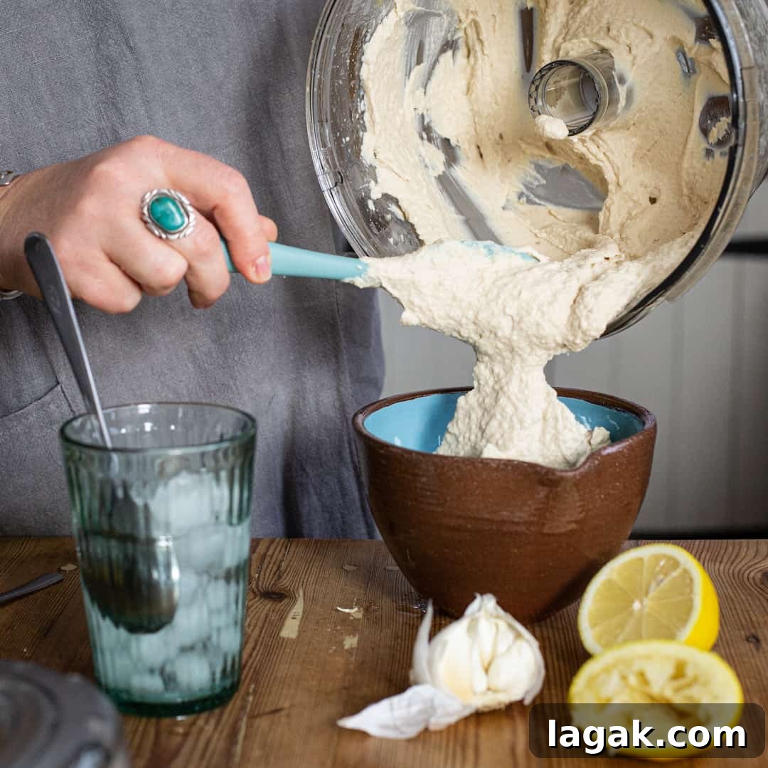 Creamy Vegan Butter Bean Dip — Protein-Packed Snack Recipe 11 Scraping hummus from a food processor bowl into a serving bowl