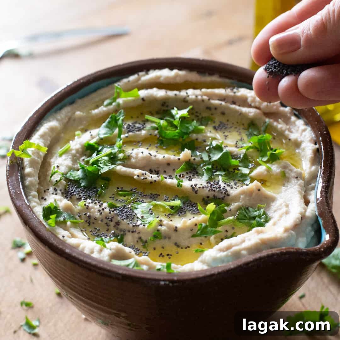 Creamy Vegan Butter Bean Dip — Protein-Packed Snack Recipe 14 Hand sprinkling chopped parsley on top of a bowl of butter bean hummus