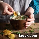 Creamy Vegan Butter Bean Dip — Protein-Packed Snack Recipe 16 Woman's hands scooping butter bean dip from a brown bowl on a wooden kitchen counter