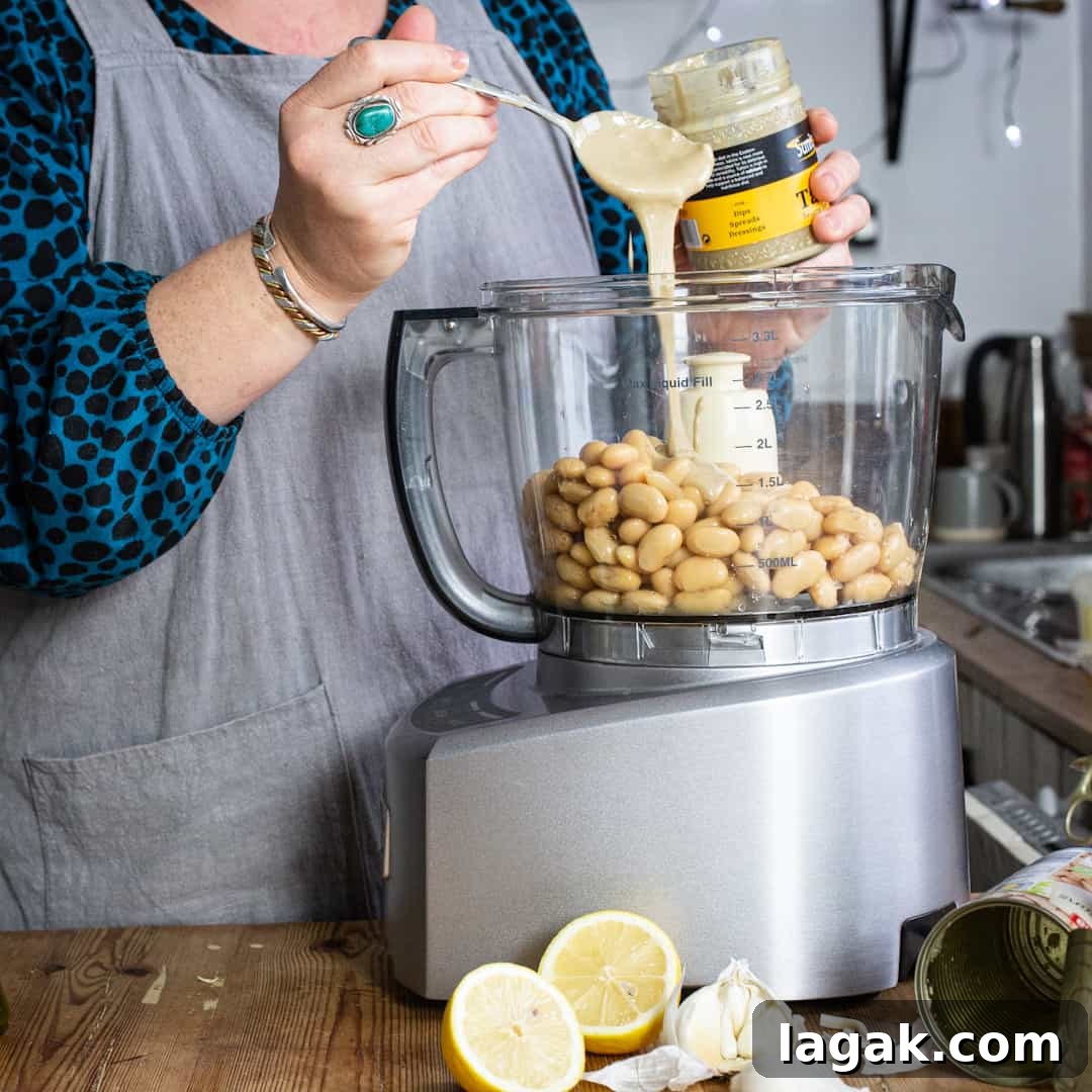 Creamy Vegan Butter Bean Dip — Protein-Packed Snack Recipe 4 Woman pouring tahini from a silver spoon into a food mixer