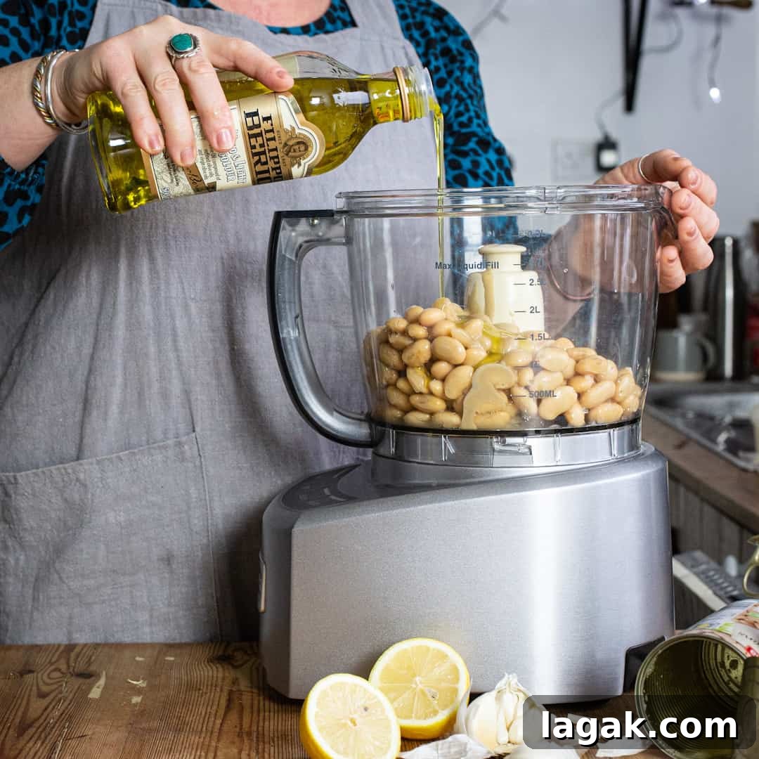 Creamy Vegan Butter Bean Dip — Protein-Packed Snack Recipe 5 Woman pouring olive oil into a food processor filled with butter beans