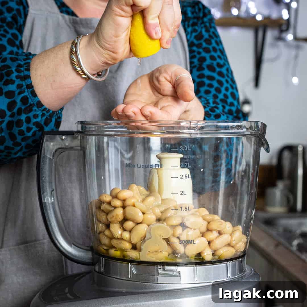 Creamy Vegan Butter Bean Dip — Protein-Packed Snack Recipe 6 Woman squeezing a lemon into a mixer of hummus ingredients