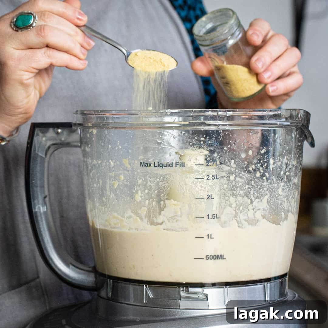 Creamy Vegan Butter Bean Dip — Protein-Packed Snack Recipe 8 Hands tipping dried garlic granules into a processor filled with homemade butter bean dip