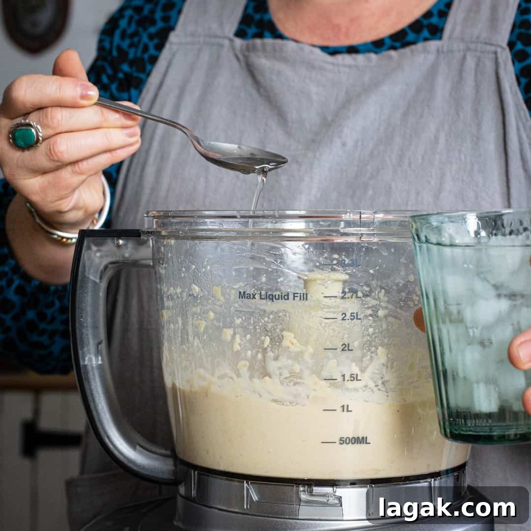 Creamy Vegan Butter Bean Dip — Protein-Packed Snack Recipe 10 Spoon of ice water being added to a food processor