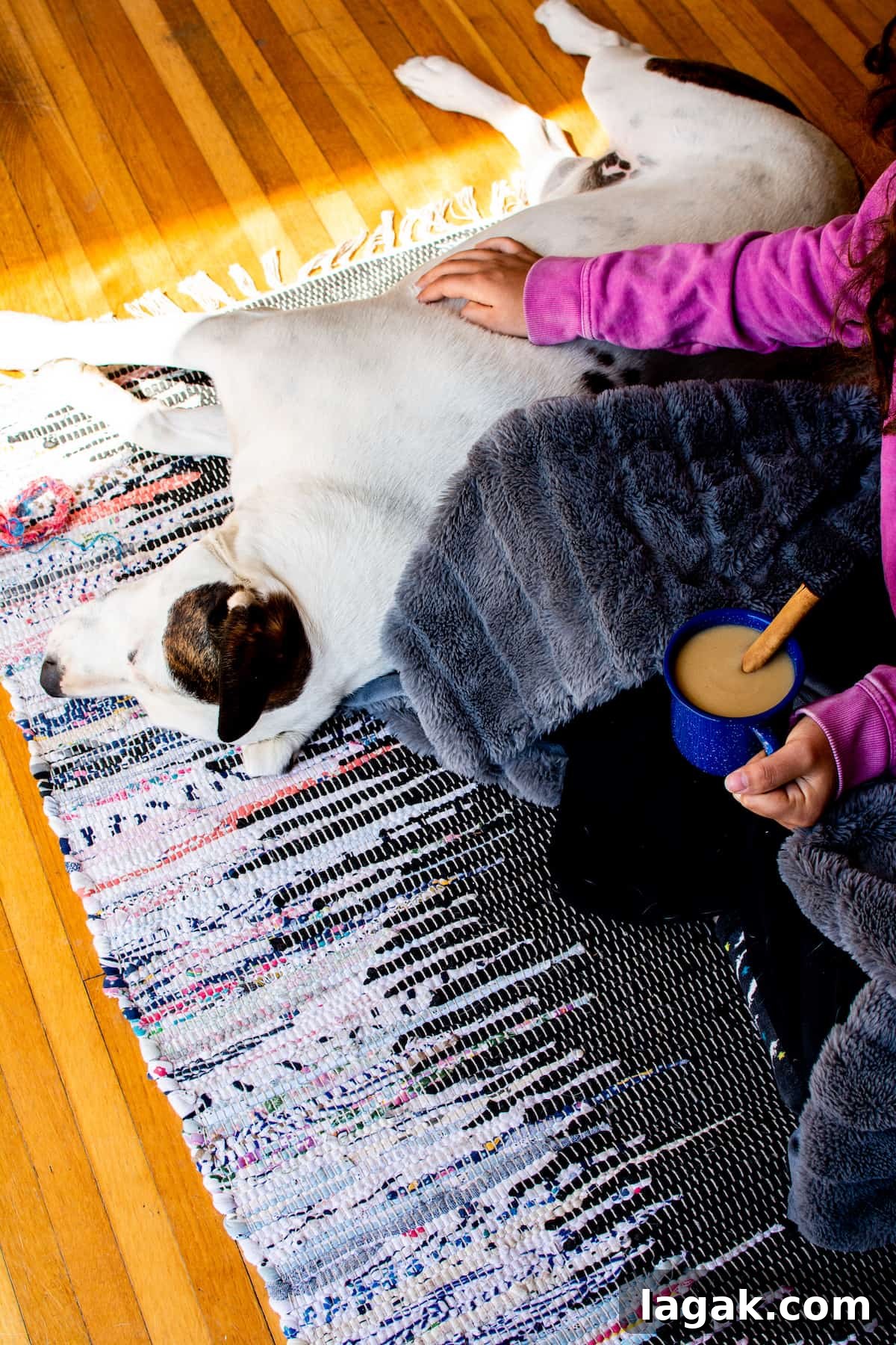 Vegan Atole: Warm Cinnamon Corn Drink Recipe 2 A girl and a dog sitting on a rug on the floor. The girl has a blanket wrapped around her and is holding a mug of atole.