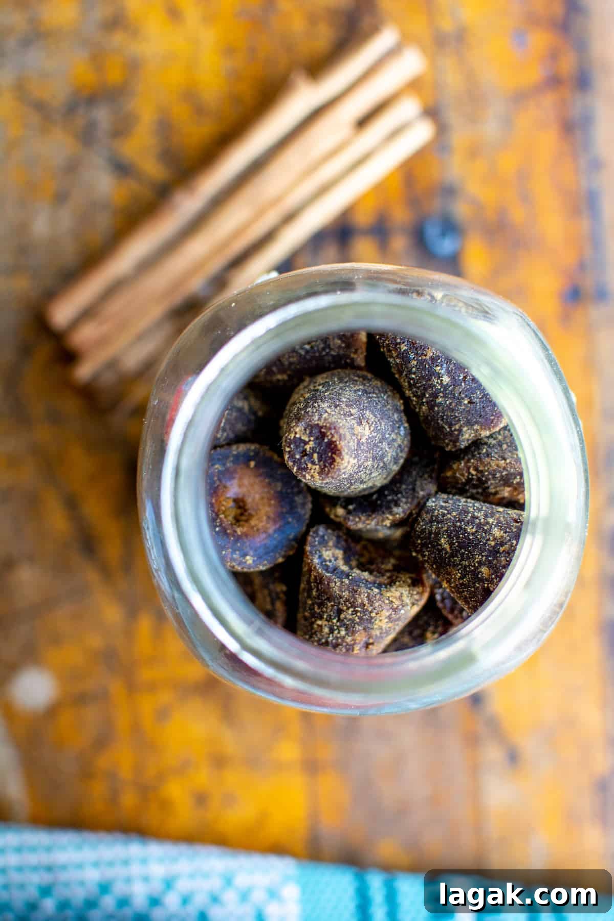 Vegan Atole: Warm Cinnamon Corn Drink Recipe 5 Cones of piloncillo, a raw cane sugar, in a large Mason jar with the lid off sitting on a wood table next to some sticks of cinnamon.