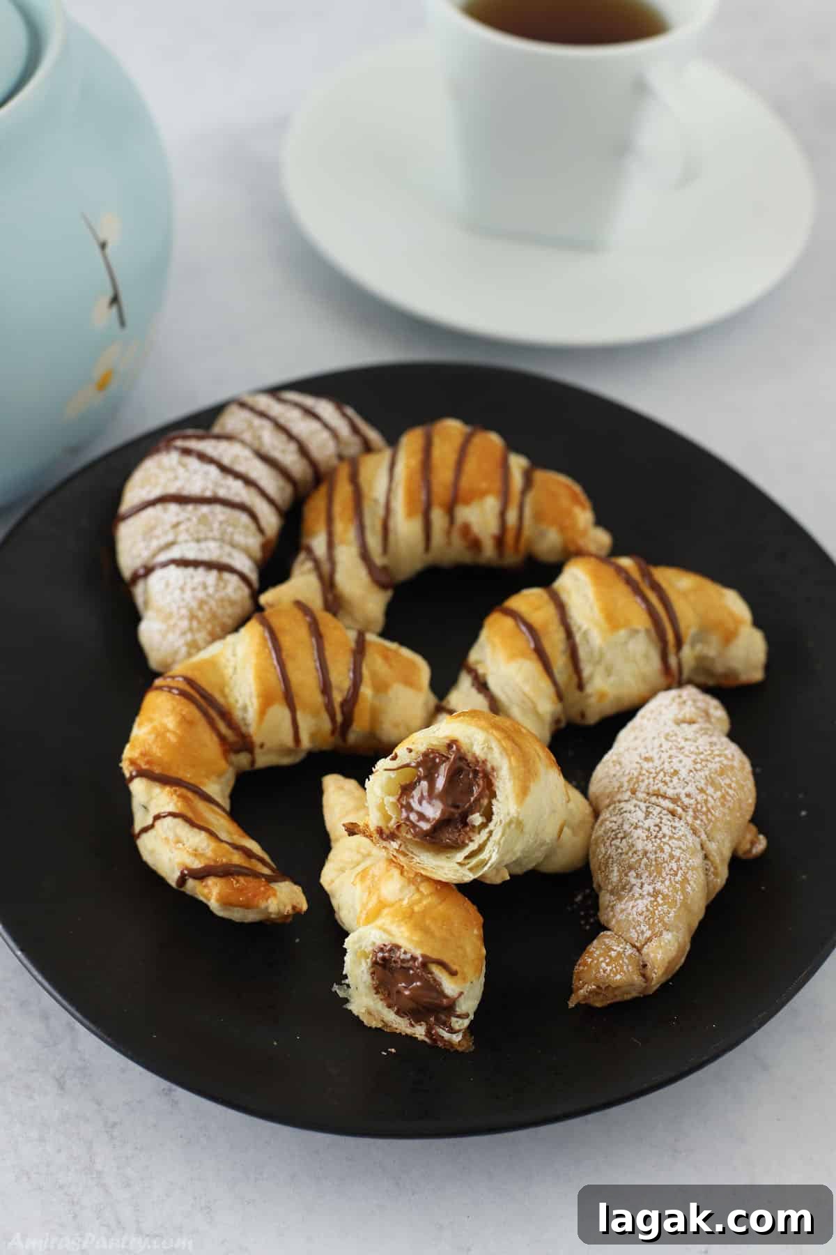 How to Make Classic Chocolate Croissants (Pain au Chocolat) 6 Chocolate croissants on a black serving plate with one cut in half to show melted chocolate.