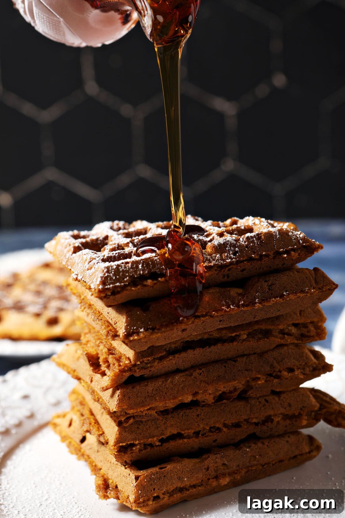 Pumpkin Waffles with Cinnamon Maple Syrup Recipe 2 Syrup pours onto a stack of pumpkin waffles on a white plate