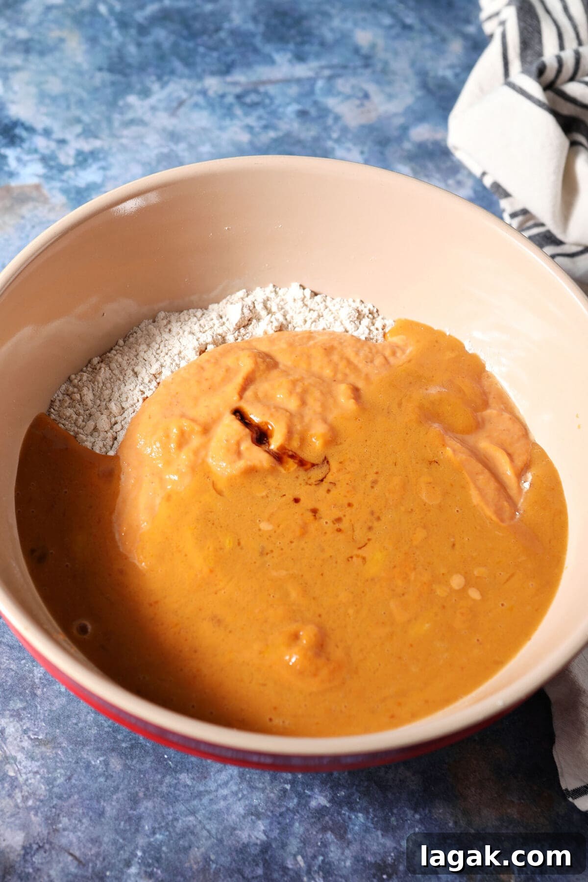 Pumpkin Waffles with Cinnamon Maple Syrup Recipe 7 Wet ingredients sit on top of dry ingredients in a bowl on a dark blue surface before mixing