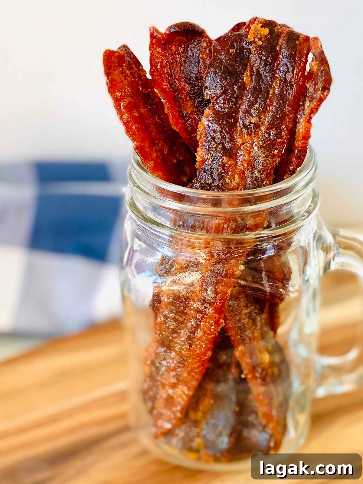 Savory Bacon Jerky: Homemade Recipe and Cooking Tips 2 candied bacon jerky sitting upright in glass jar with blue napkin in background