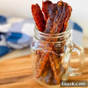 Savory Bacon Jerky: Homemade Recipe and Cooking Tips 6 bacon jerky sitting upright in glass jar with blue napkin in background