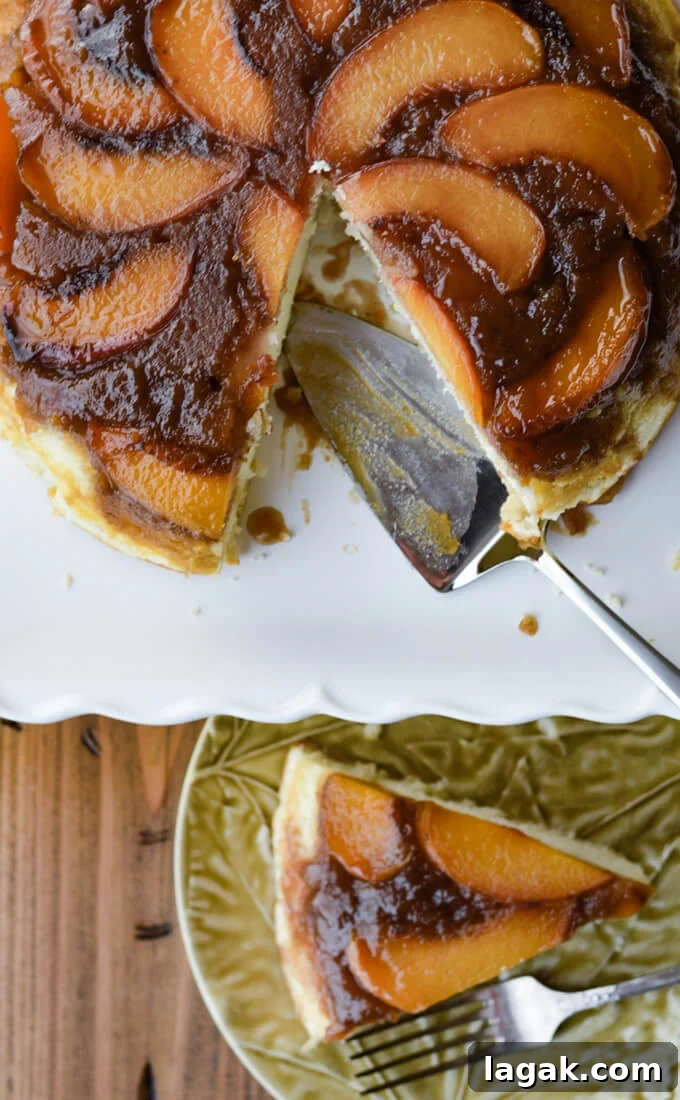 Caramelized Fresh Peach Upside-Down Cake Recipe for Summer 9 A peach upside down cake on a white cake platter with a piece cut out. The piece is on a plate beneath the platter.