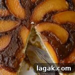 A close-up photo a peach upside down cake wit a cake server in the pan. A pieces has been taken out.