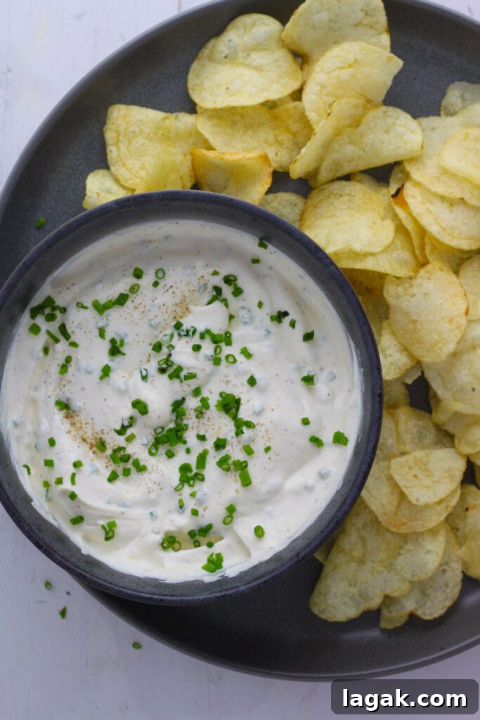 Creamy Sour Cream & Chive Dip Recipe for Parties 2 A blue bowl with sour cream and chive dip and a plate of potato chips.