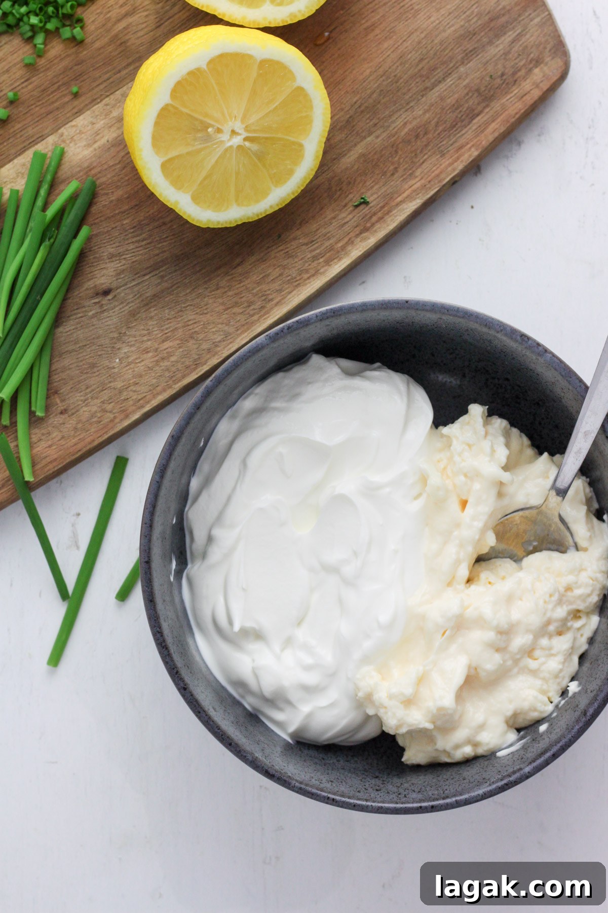 Creamy Sour Cream & Chive Dip Recipe for Parties 4 A blue bowl with sour cream and mayonnaise and a cutting board with a lemon.
