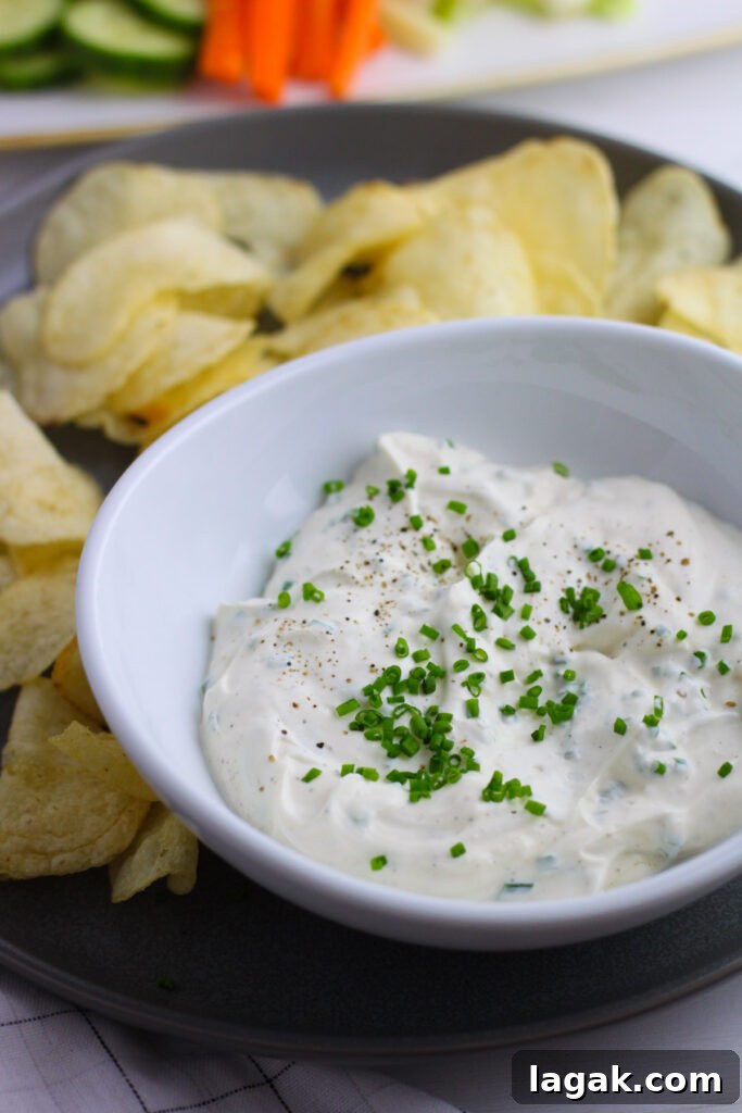 Creamy Sour Cream & Chive Dip Recipe for Parties 7 A white bowl with sour cream and chive dip and a plate of potato chips.