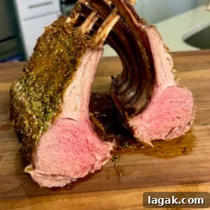 Garlic and Herb Roasted Rack of Lamb Recipe for Juicy Results 11 A perfectly cooked rack of lamb cut into two sections, displaying a pink, juicy interior and seasoned crust, resting on a wooden cutting board in a kitchen setting.