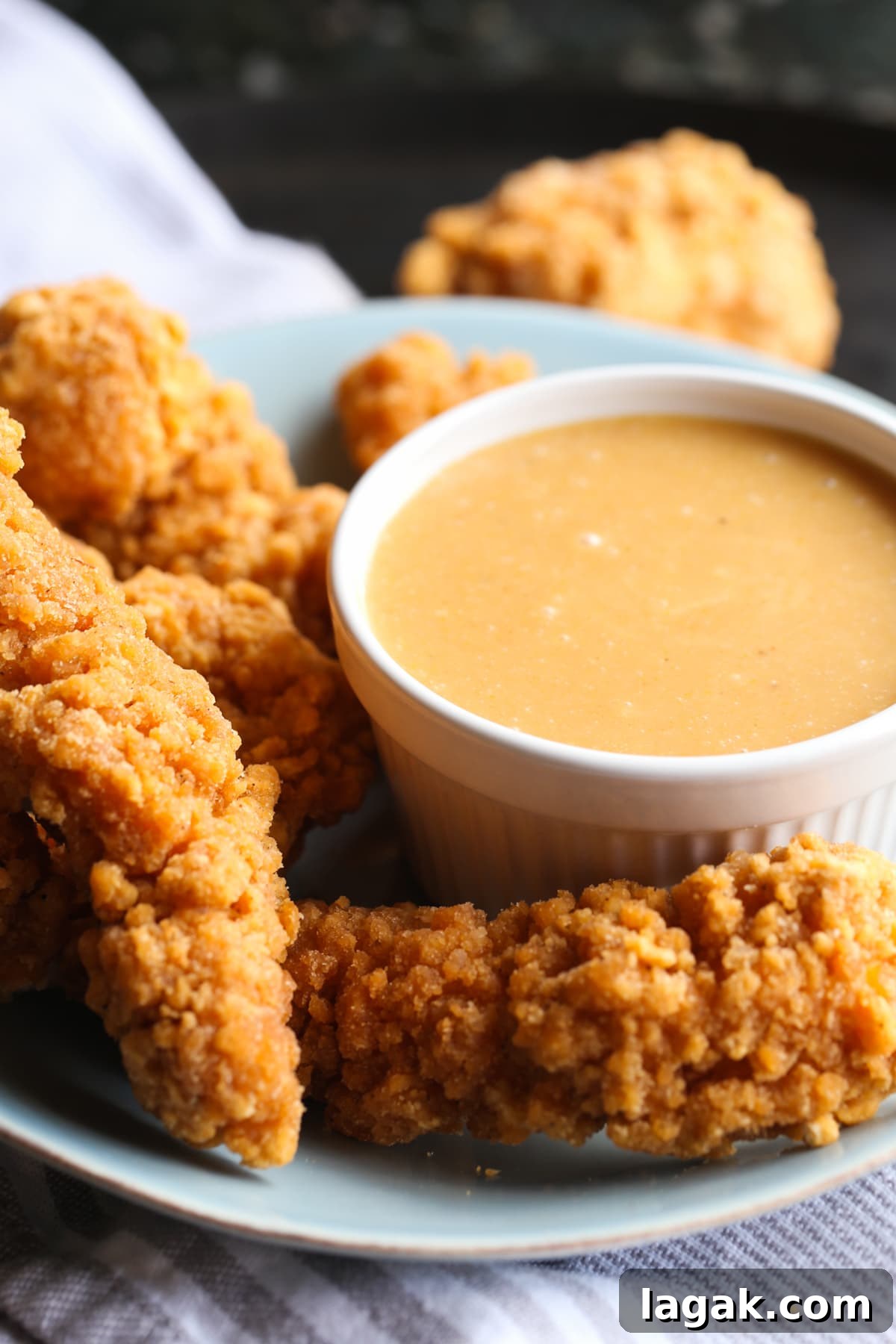This Chick Fil A Sauce recipe is the BEST Chicken Dipping Sauce! Smoky, sweet, with a slight tang, it's PERFECT for dipping chicken nuggets, grilled chicken, or french fries! A bowl of homemade chicken dipping sauce on a plate with breaded and fried chicken tenders