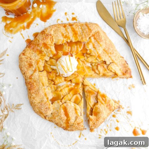 Caramel Apple Galette Recipe: Rustic Fall Dessert with Salty Caramel 24 caramel apple galette with scoop of ice cream on top on parchment paper with slice on plate beside, gold leaf garland and jar of caramel to the left side, and fork and knife to the right side