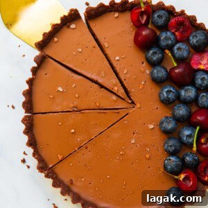 Decadent Vegan Chocolate Tart Recipe for Rich, Creamy Desserts 10 overhead of vegan chocolate tart sliced with golden cake slice and topped with berries.