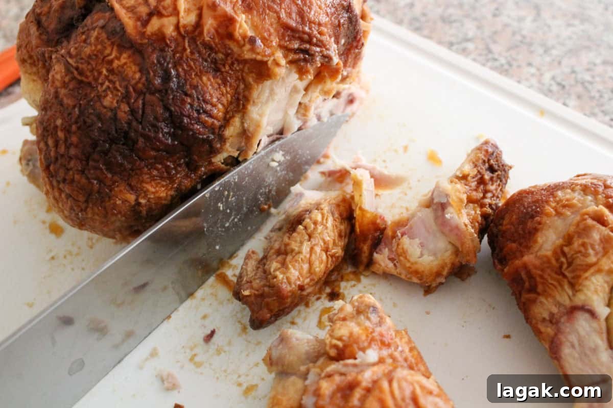 How to Cut and Shred Rotisserie Chicken: Portioning & Freezing Tips 6 A close-up of a large knife slicing roasted chicken on a white cutting board, with pieces of chicken and crispy skin scattered nearby.