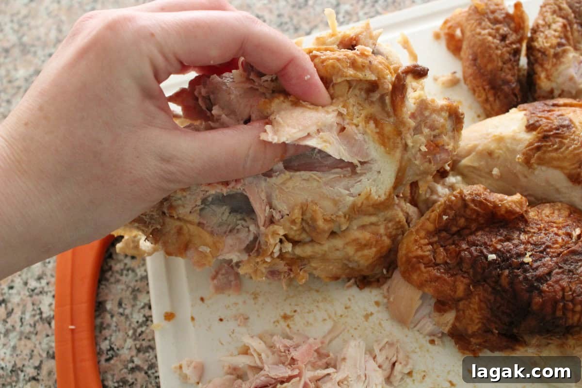 How to Cut and Shred Rotisserie Chicken: Portioning & Freezing Tips 8 A hand is shredding cooked chicken on a white cutting board with pieces of chicken and skin nearby.