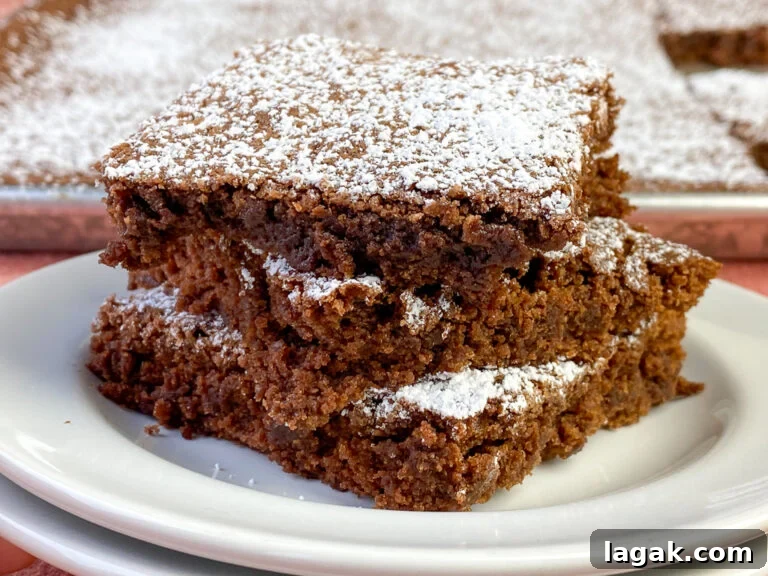 Stack of three large brownies on a small white plate in front of a large sheet pan of brownies