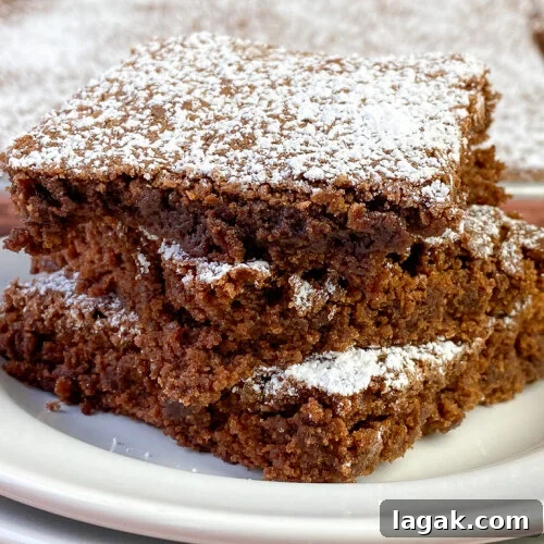 Close up moist brownies stacked up with a thin layer of powdered sugar on top of each piece